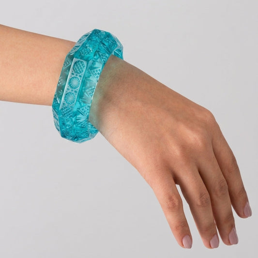 A translucent turquoise blue bangle bracelet with a textured geometric pattern, shown worn on a person's wrist against a plain light gray background.