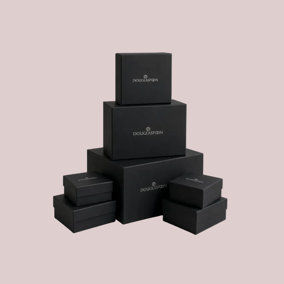 A stack of black Douglasspan jewelry boxes in various sizes, arranged in a pyramid-like structure on a light beige background.