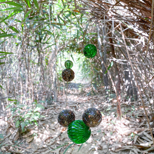 a long green and grey textured bead necklace hanging from a tree branch in a bamboo forest.