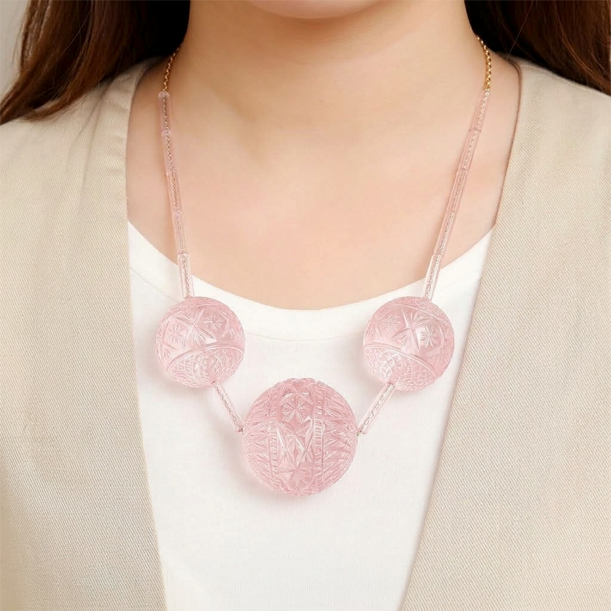 A close-up of a model wearing a pink translucent statement necklace with three carved circular pendants and delicate chain straps.