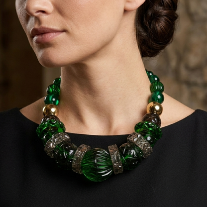 A close-up of a woman wearing a chunky statement necklace made of green glass beads, textured dark green beads, and metallic gold and silver spacer rings, paired with a black sleeveless top.