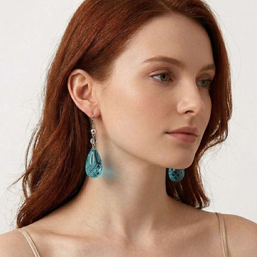 Woman wearing blue teardrop earrings against a plain background