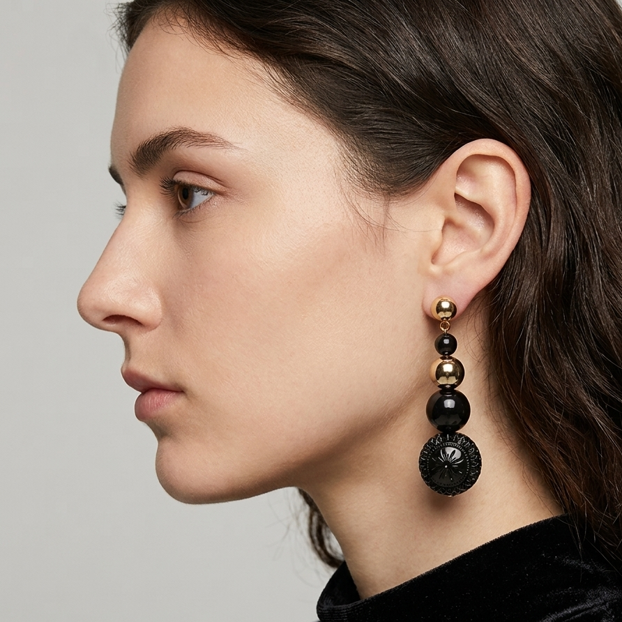 A close-up side profile of a woman wearing a long, multi-tier beaded drop earring. The earring features alternating polished gold and matte black beads, culminating in a large textured black disc pendant.
