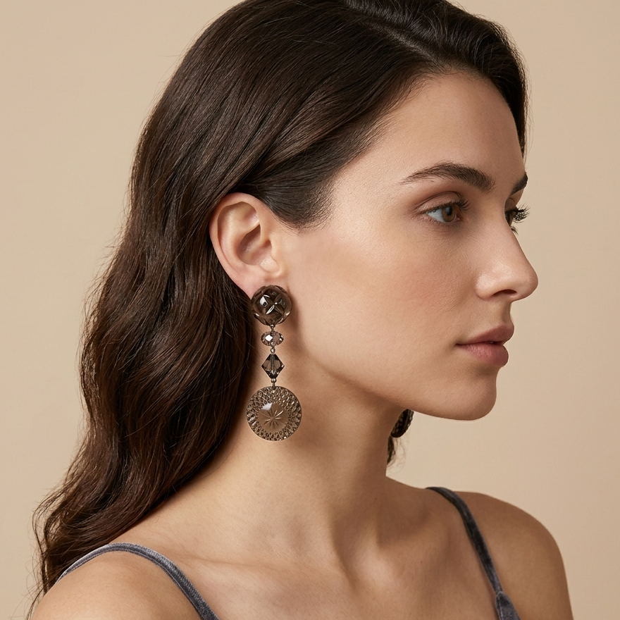 A woman in profile wearing a long, ornate bronze-toned dangle earring with circular and geometric details, set against a solid beige background.