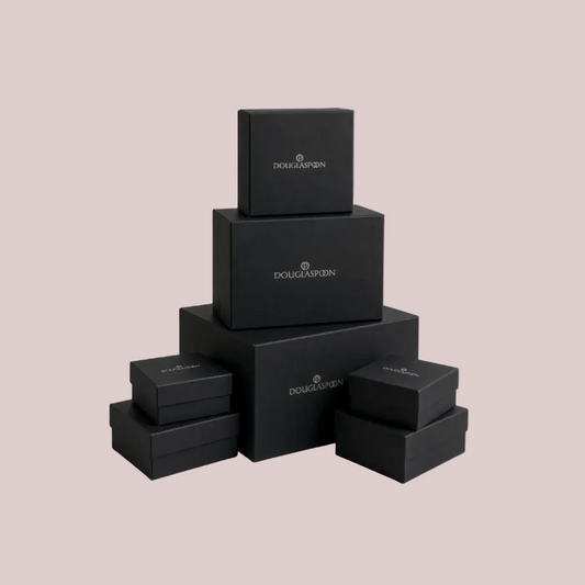 A stack of black Douglasspan jewelry boxes in various sizes, arranged in a pyramid-like structure on a light beige background.